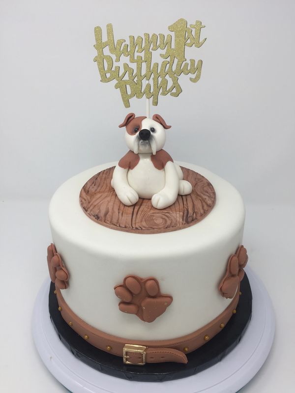 White cake with English bulldog on top and dog prints on side.