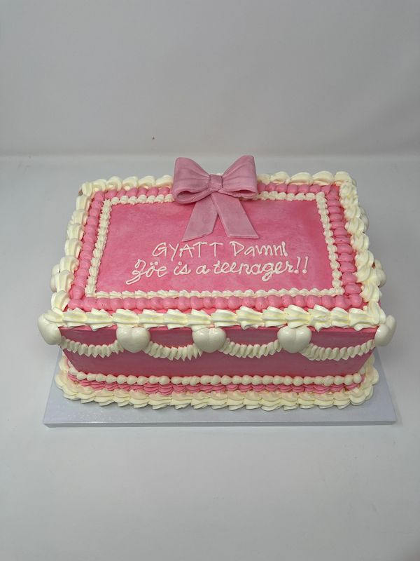 Pink cake with white garlands and hearts and a pink bow.