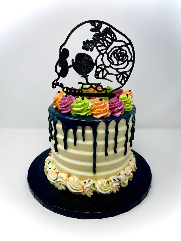 Cake with black drip and multi colored rosettes an a black outline skull on top
