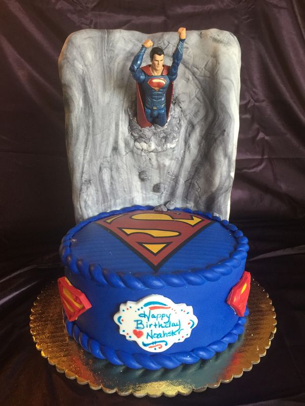 blue cake with Superman logo and toy Superman coming out of gray wall
