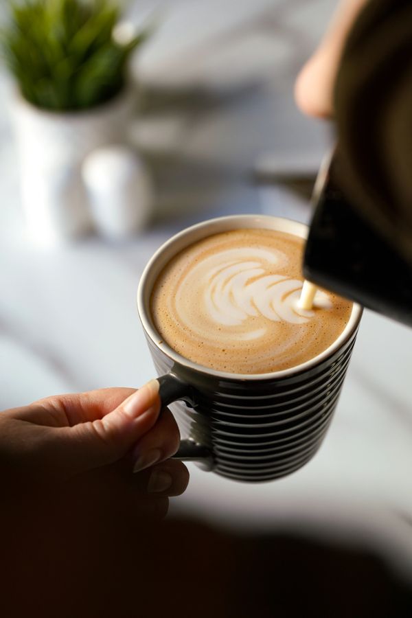 Pouring milk into coffee creating latte art in a striped mug.