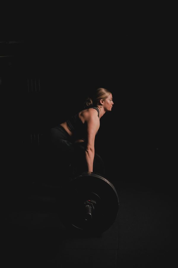 Woman lifting a barbell in a dimly lit gym.