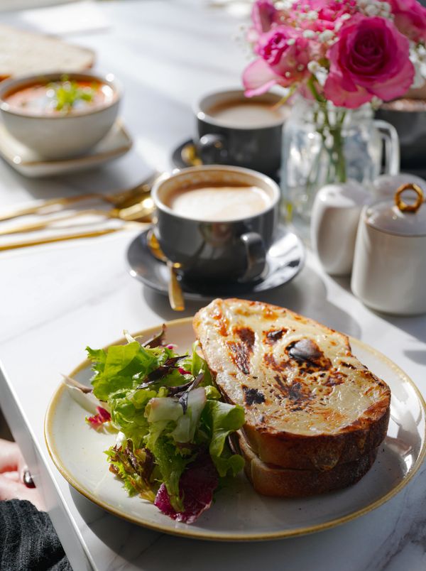 Grilled cheese sandwich with fresh salad on a white plate, accompanied by coffee cups and flowers.