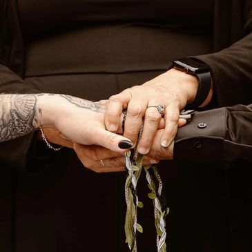 Two hands holding each other with braided cords and a tattoo visible on one arm.