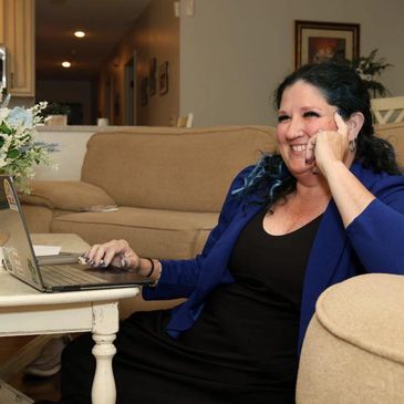 Woman smiling while using a laptop at home, sitting on the floor by a coffee table.