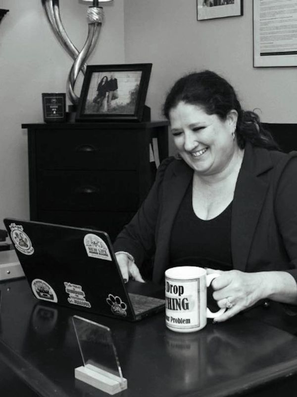 Smiling woman working on laptop at desk with coffee mug in hand.
