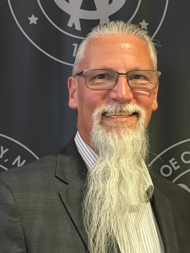 Smiling man with glasses and a long white beard in a suit.