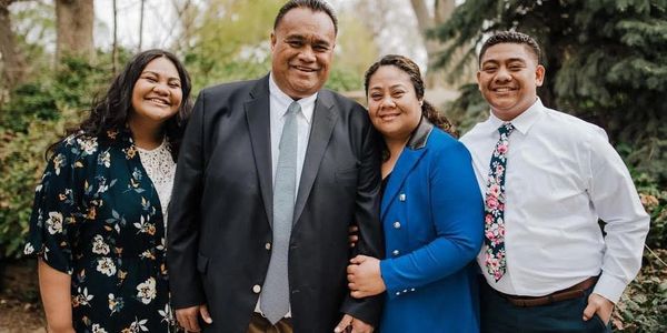 A smiling family of four posing outdoors in formal attire.