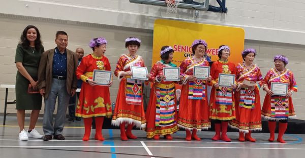 Group of elderly women in traditional dresses holding certificates.