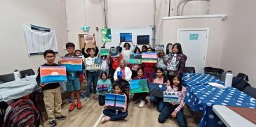 Group of children proudly showing their paintings in a classroom.