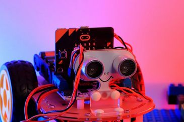 A small robot with sensors and wires under colorful lighting.
