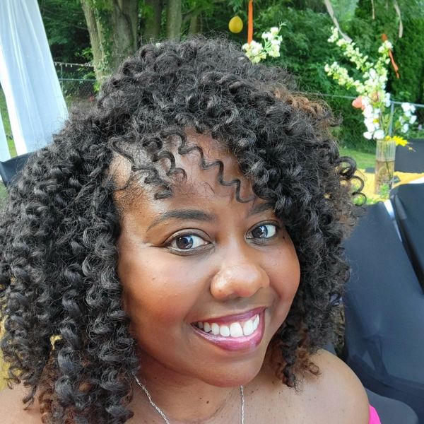 Smiling woman with curly hair at an outdoor event with floral decorations.