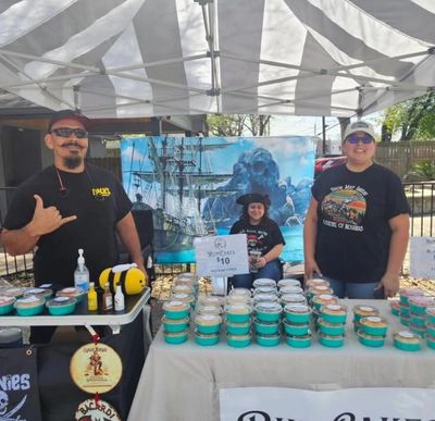 Three people selling rum cakes under a tent with a pirate backdrop.