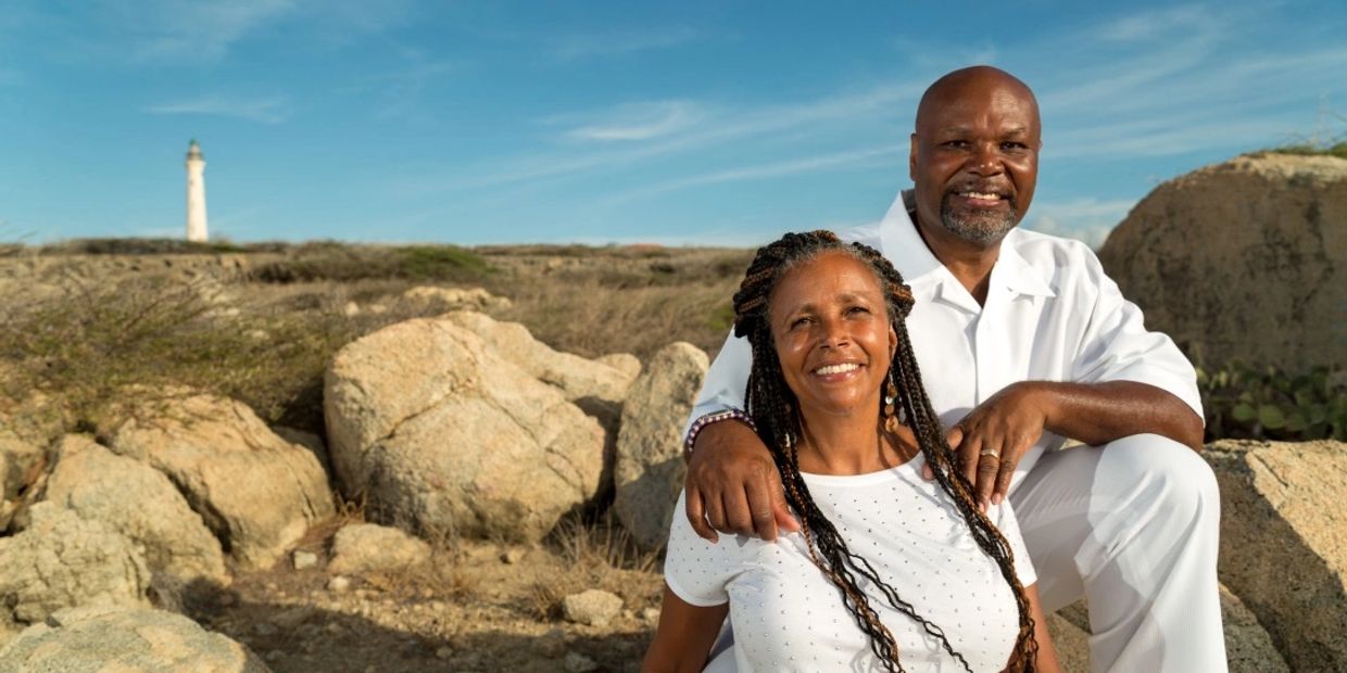 Picture of Drs. William & Paula Smith in white sitting on rocks with lighthouse in the background 