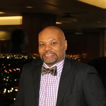 Dr. Smith posing for a photo at event (sitting in front of window with night skyline blurred behind)