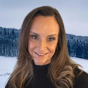 Smiling woman with long hair in front of a snowy forest landscape.