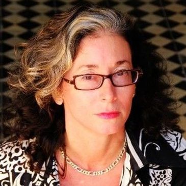 Woman with curly hair and glasses in patterned clothing.