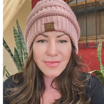 Woman wearing a pink knit beanie smiling gently.