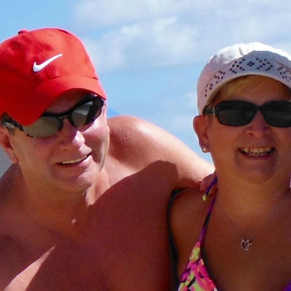 A smiling couple wearing sunglasses and hats at the beach.