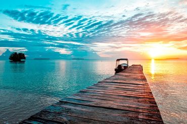 Wooden pier extending into calm sea at sunset with a boat docked.