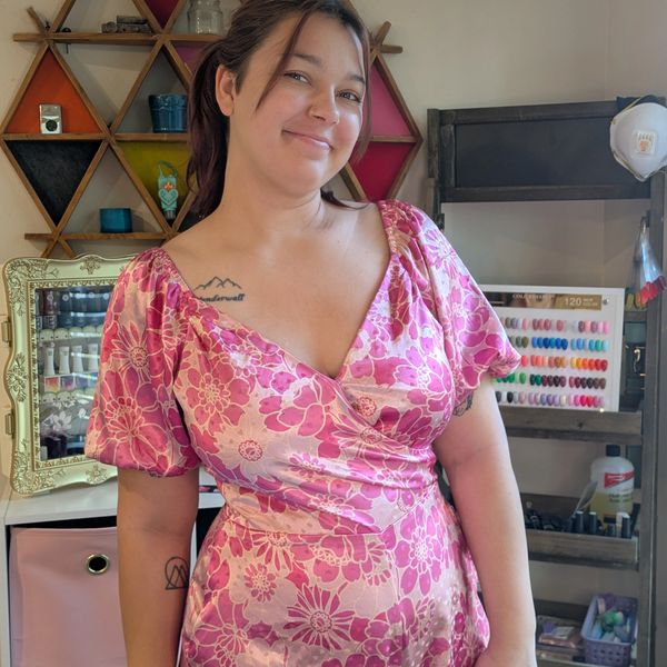 Woman in a pink floral dress smiling indoors.