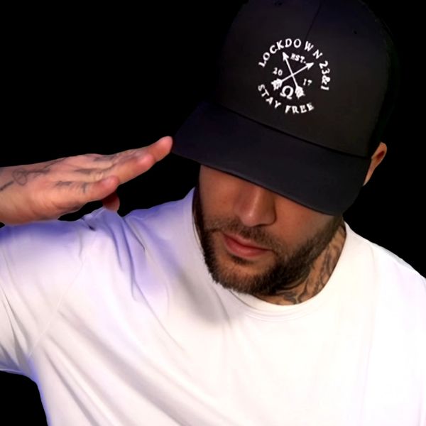 Man in white shirt saluting, wearing black cap with 'Lockdown' text.