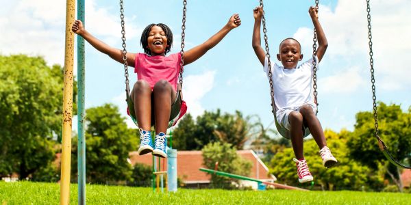 Two children joyfully swinging in a sunny park.