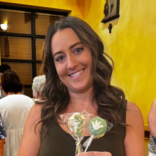 Woman smiling, holding decorated cookies with religious designs.