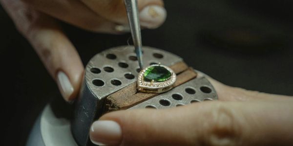 A person working on setting a green gemstone in jewelry.