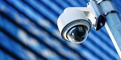 A white security camera mounted on a pole with a blue-striped background.