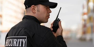 Security guard using a walkie-talkie outdoors in uniform.