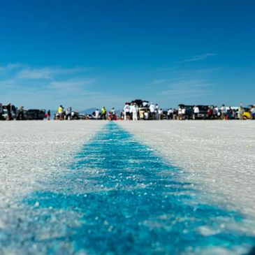 Low-angle view of a blue line on a salt flat with cars and people in the distance.