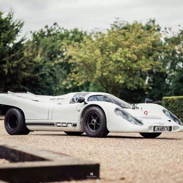 White Icon 917K race car parked on gravel with trees in background.