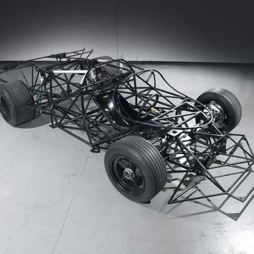 Exposed frame of a race car chassis with seat and wheels.