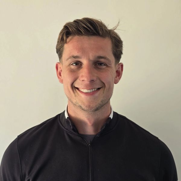 Smiling young man in a black jacket against a plain background.