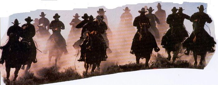 men (cowboys) ride on horseback as the sun is setting. the ground is dusty