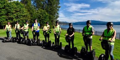 Group of people riding Segways near a waterfront on a sunny day.
