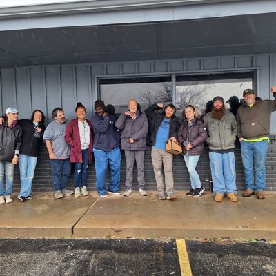 A group of ten people posing outside a building on a rainy day.