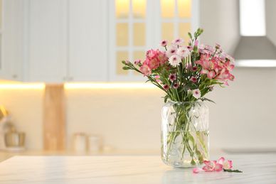 A bouquet of pink and white flowers in a glass vase on a kitchen counter.