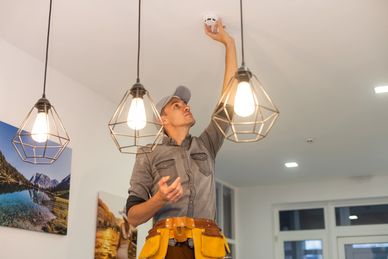 Technician installing a smoke detector on the ceiling indoors.