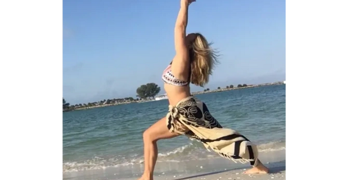Woman practicing yoga on the beach by the ocean under clear skies.