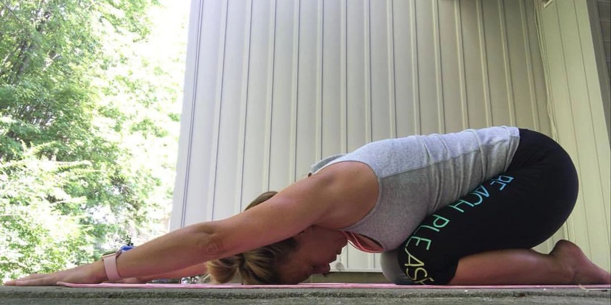 Woman practicing child's pose yoga outdoors on a mat.