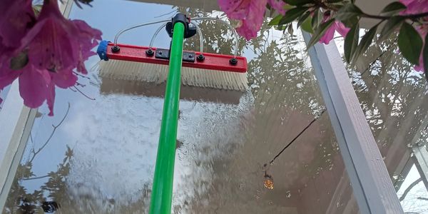 A green-handled squeegee cleaning a glass window surrounded by flowers.