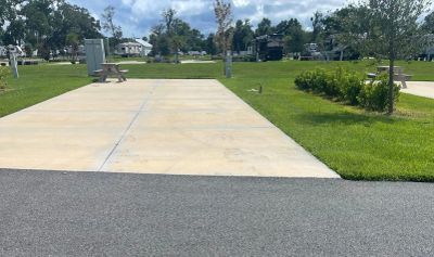 Empty concrete pad in park with grass and trees.