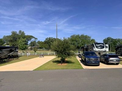 A sunny RV park with parked vehicles and trailers on concrete pads.