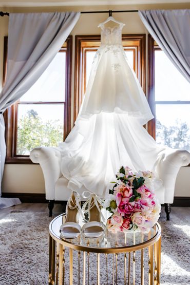 Elegant wedding dress, shoes, and bouquet displayed in a sunlit room.