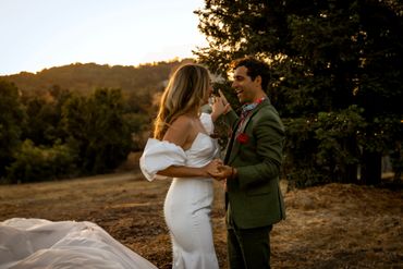 A couple shares a joyful moment outdoors at sunset, dressed in wedding attire.