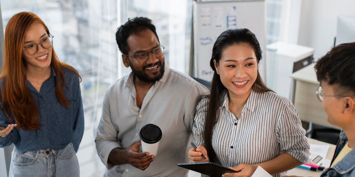 Four colleagues smiling and discussing in a bright office setting.