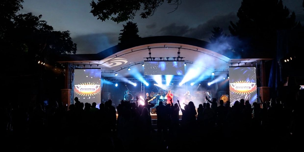 Outdoor concert at night with bright stage lights and an enthusiastic crowd.