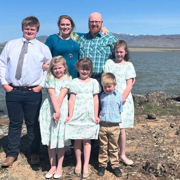 A smiling family of seven poses by a lakeside on a sunny day.